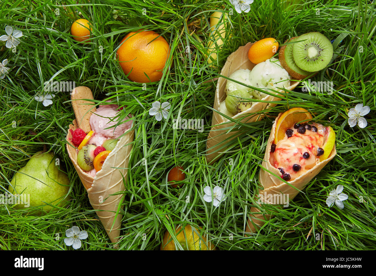 Assortiment d'été de la crème glacée aux fruits saveurs de kiwi, l'orange, les baies dans un cornet gaufré sur fond d'herbe verte, des fleurs et des fruits Banque D'Images