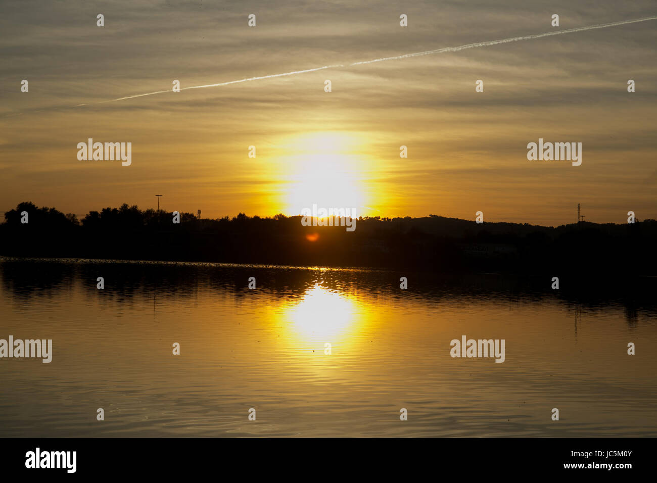 Vue sur le coucher du soleil avec des arbres et de l'eau reflet dans un lac. Banque D'Images