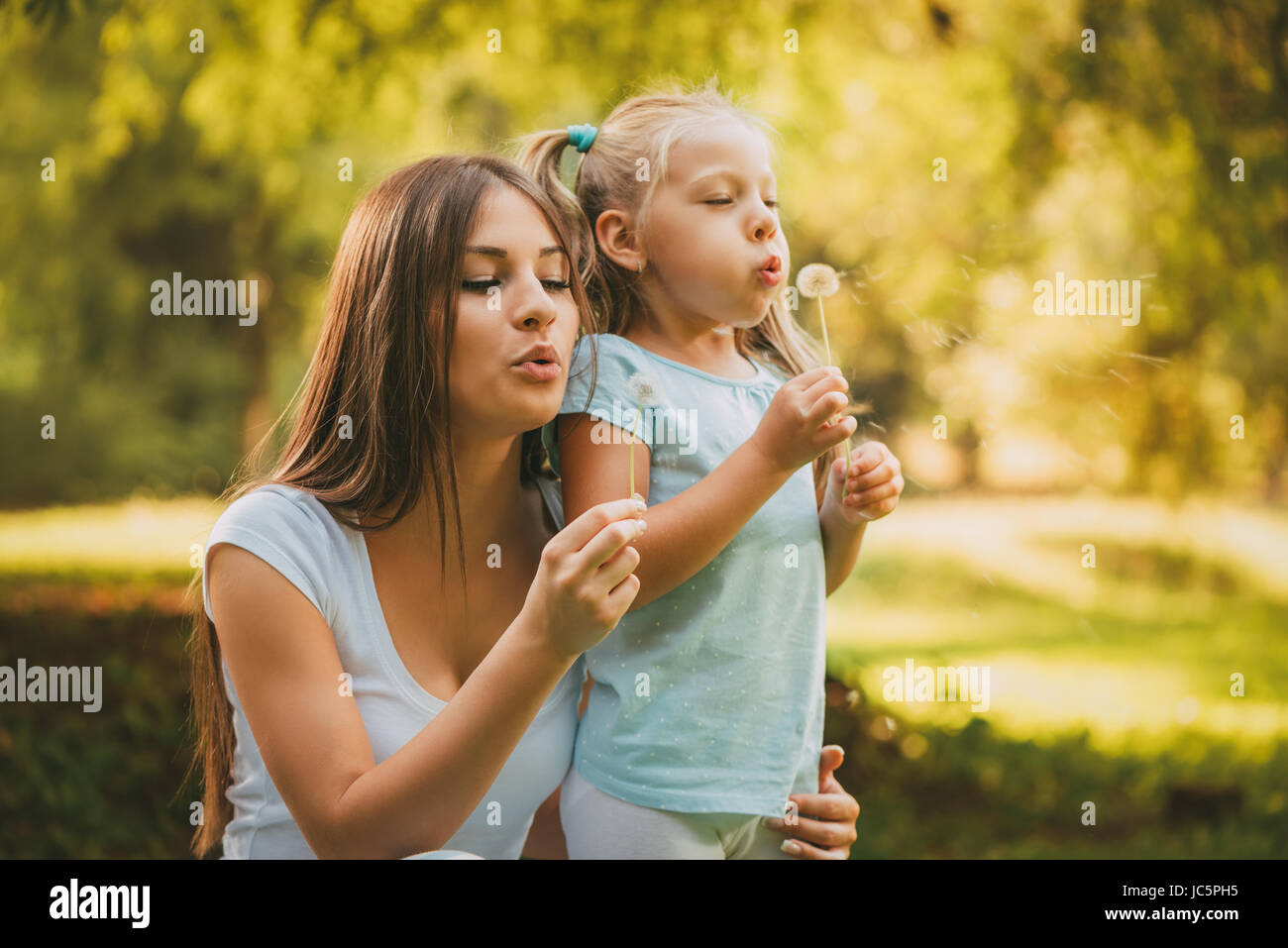 Happy cute little girl blowing dandelion avec mère dans le parc. Banque D'Images