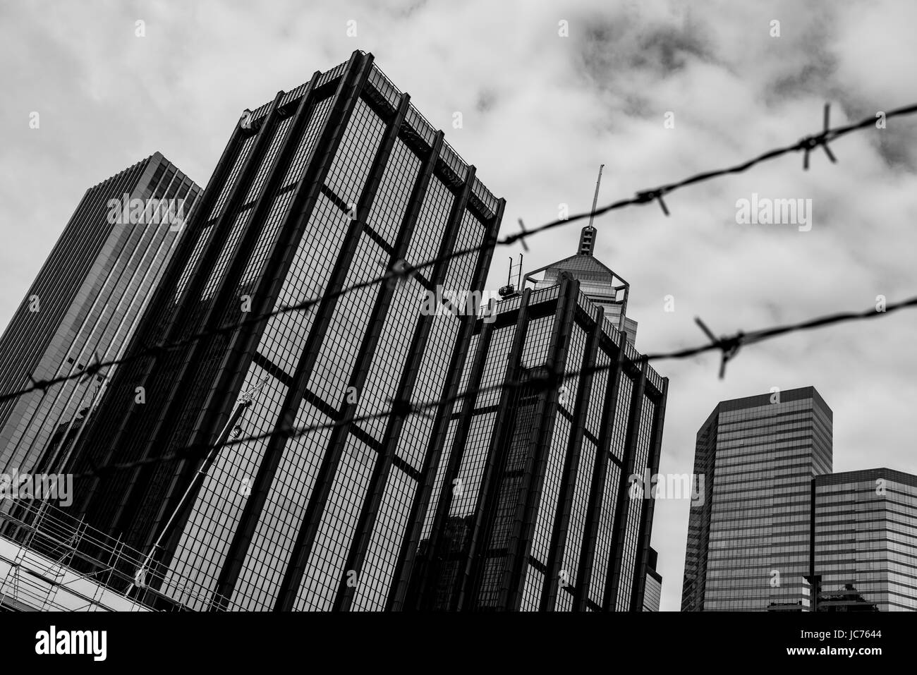 Point de vue noir et blanc d'un site de construction à Hong Kong avec d'autres grands bâtiments en arrière-plan et une clôture en fil barbelé au premier plan. Banque D'Images