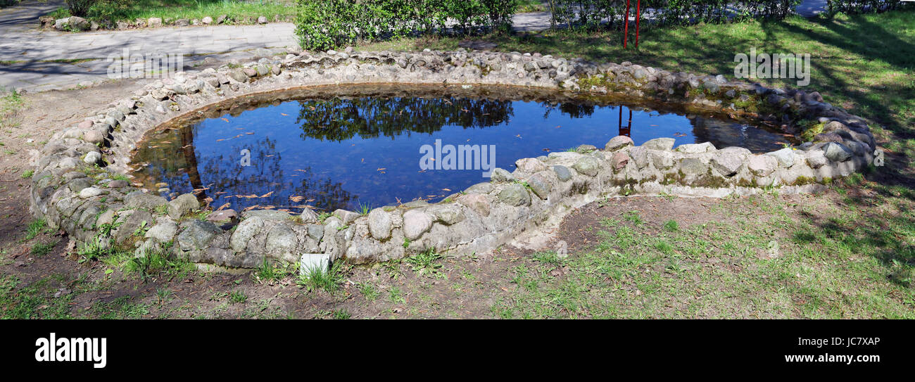 La main artificielle petit étang dans le bois de printemps. Côte de la lake sont faits de pierres de granite. Journée ensoleillée image extérieure Banque D'Images