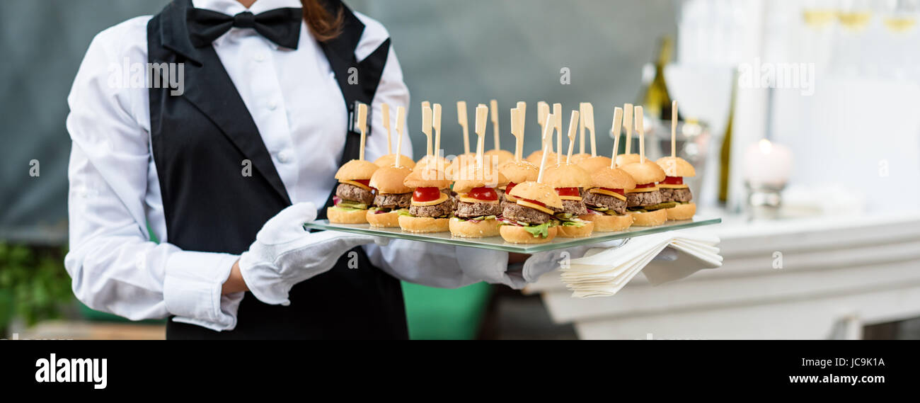 Service de traiteur. Waiter carrying un plateau de hors-d'œuvre. Partie en plein air avec la nourriture de doigt, mini-hamburgers, sliders. Banque D'Images