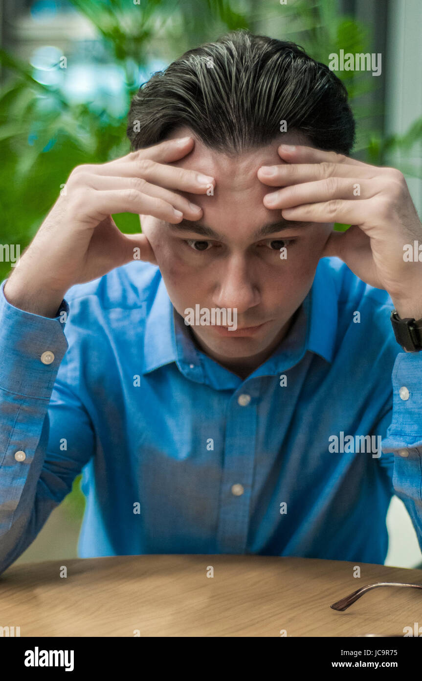 Se sentir malade et fatigué. Jeune homme frustré en gardant les yeux fermés tout en restant assis à sa place de travail social Banque D'Images