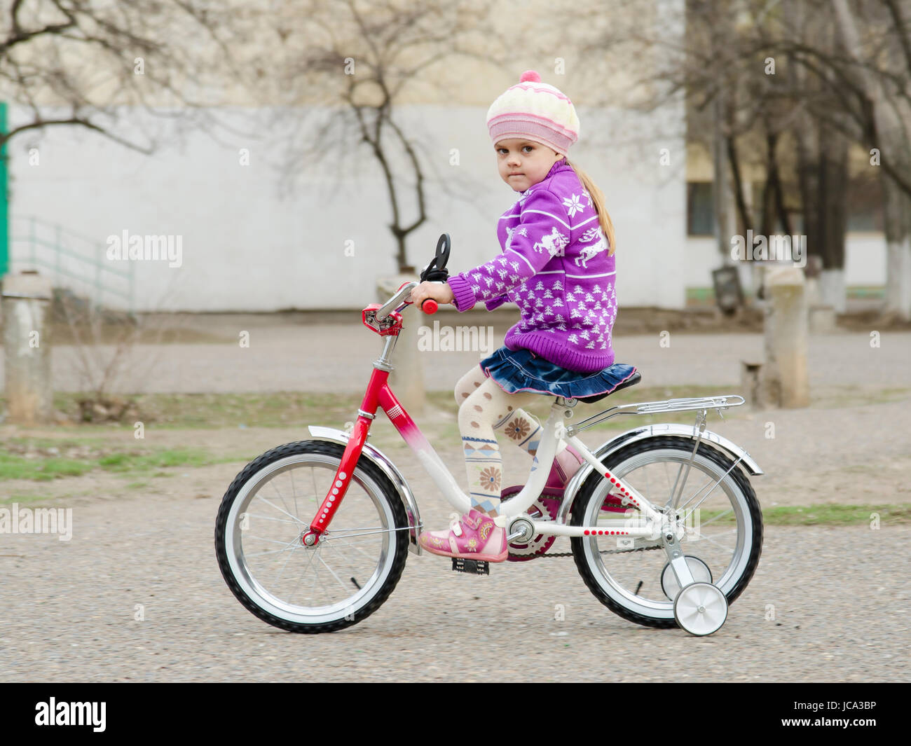 Une fillette de quatre ans va sur un vélo sur une route pavée d'asphalte. Une journée de printemps. Banque D'Images