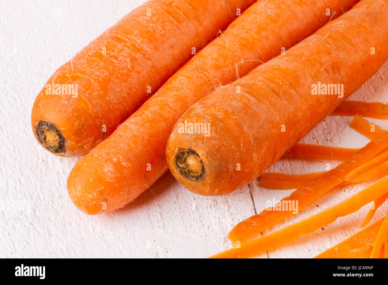 Frische orangene Karotten rüben mohrrüben geschält Sparschäler Schalen mit und auf einem Holzbrett weißer bär Banque D'Images