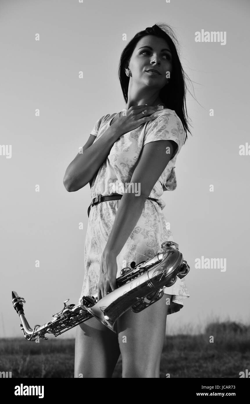 Une belle brunette dans une robe courte avec un saxophone. Une photo en noir et blanc Banque D'Images