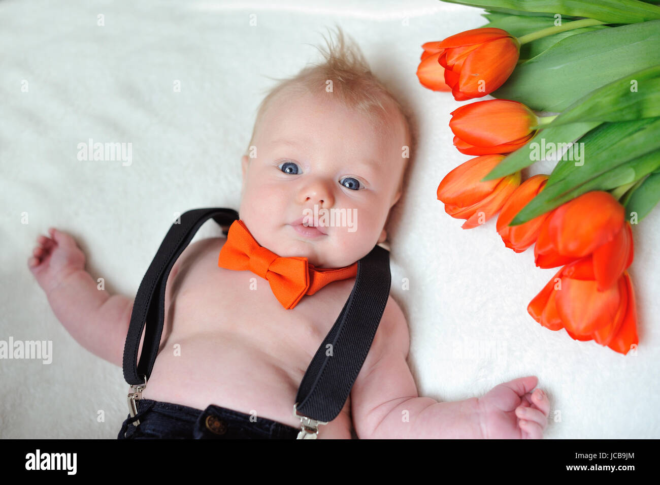 Petit garçon avec un papillon orange et un bouquet de fleurs se trouve sur le lit Banque D'Images