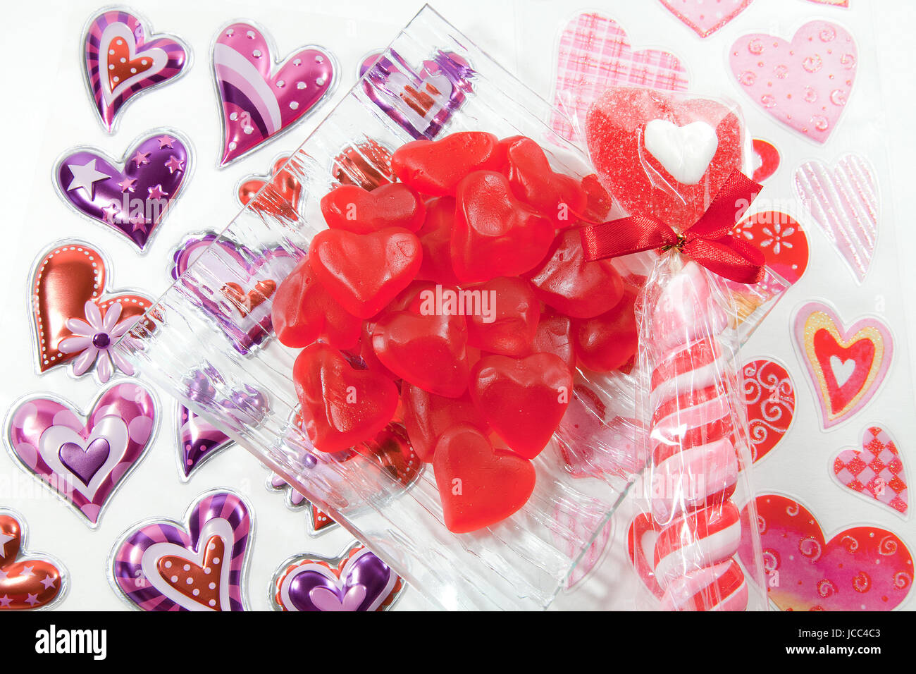Bol de bonbons coeur rouge sur une surface blanche couverte de coeur autocollants. Banque D'Images