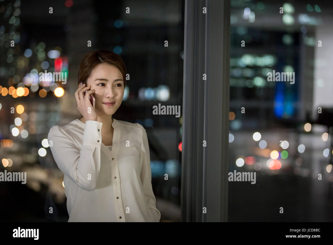 Smiling businesswoman talking on cellphone au travail de nuit Banque D'Images