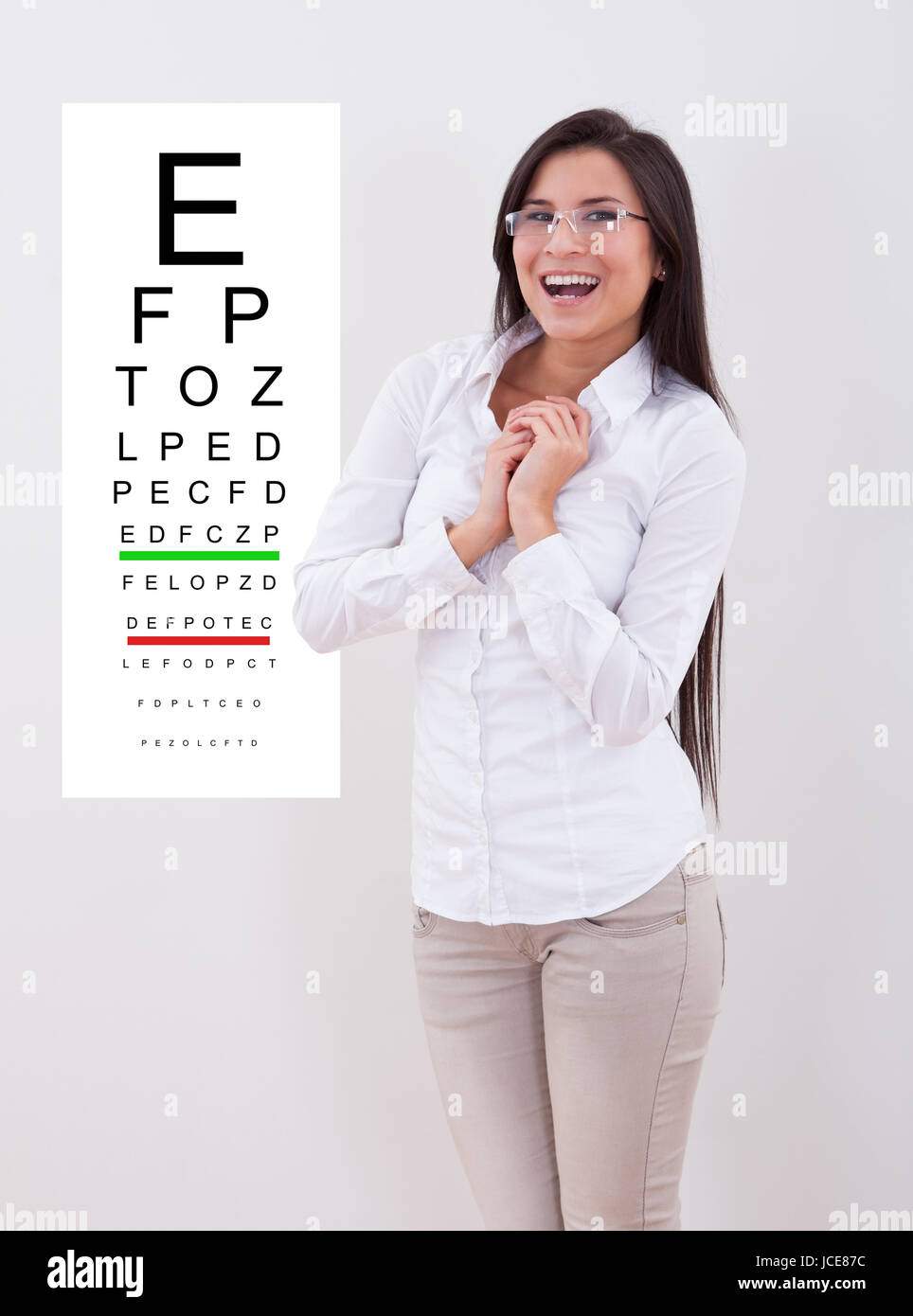 Jubilant dame avec de nouvelles lunettes, debout devant un tableau d'opticiens test oculaire monté sur un mur Banque D'Images