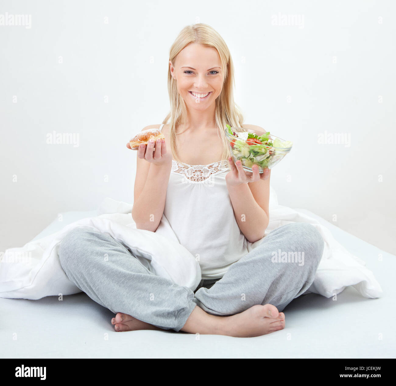 Jeune femme tentée de faire un choix entre la salade et donut Banque D'Images