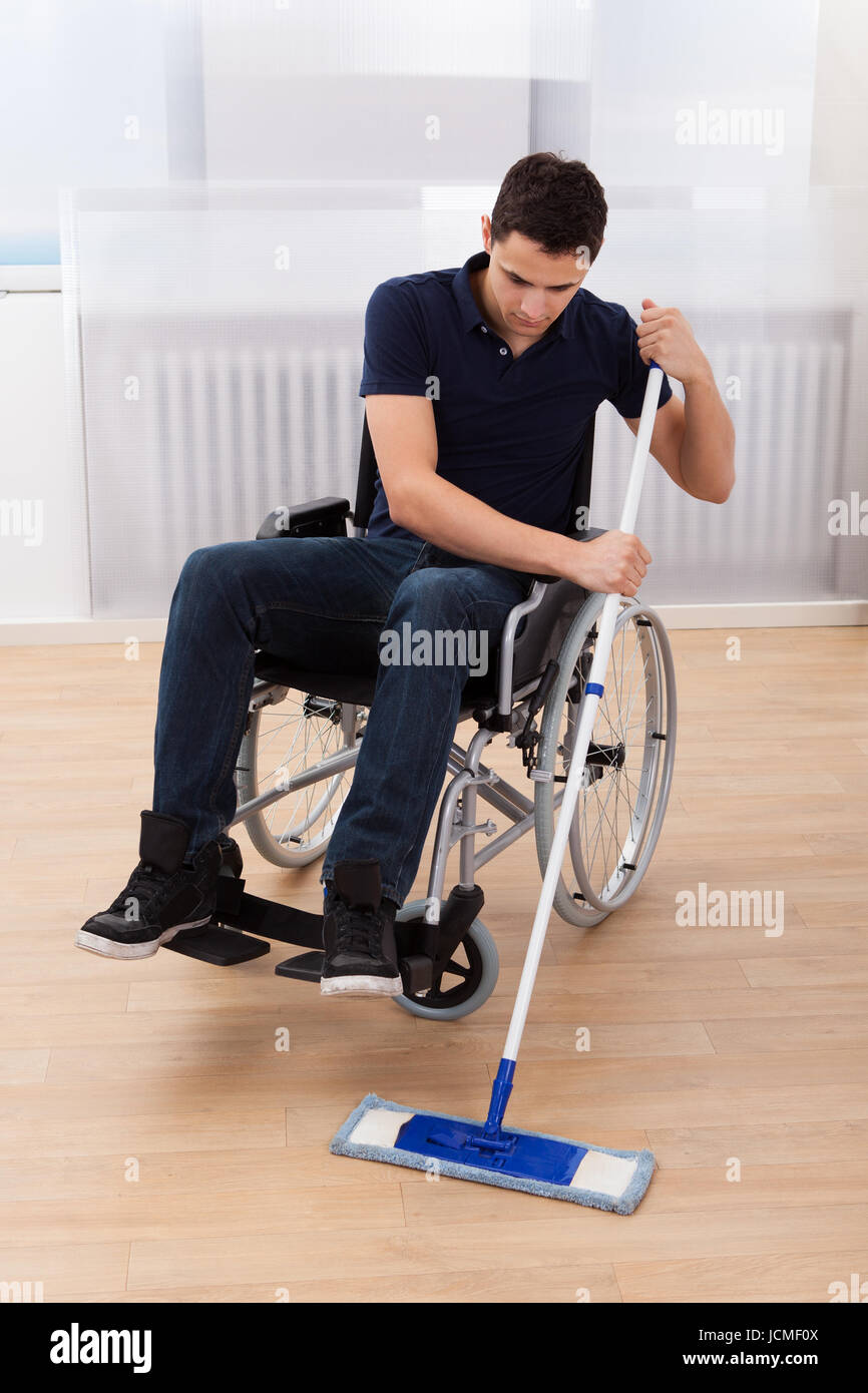 Toute la longueur du jeune homme handicapé plancher de bois dur de nettoyage  tout en restant assis sur fauteuil roulant dans chambre Photo Stock - Alamy