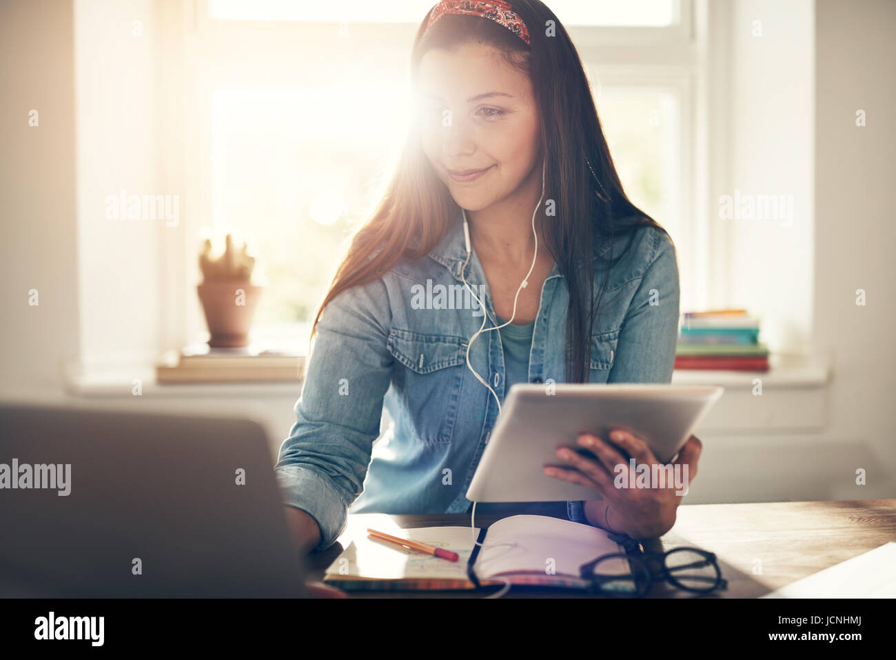 Cheerful young entrepreneur woman using laptop in earphones et holding tablet sitting in office. Banque D'Images