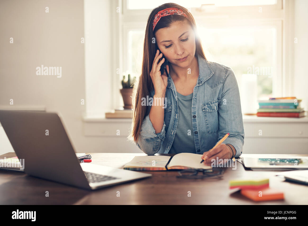 Jeune entrepreneur femme parlant smartphone et écrit dans le bloc-notes sitting at laptop in office. Banque D'Images