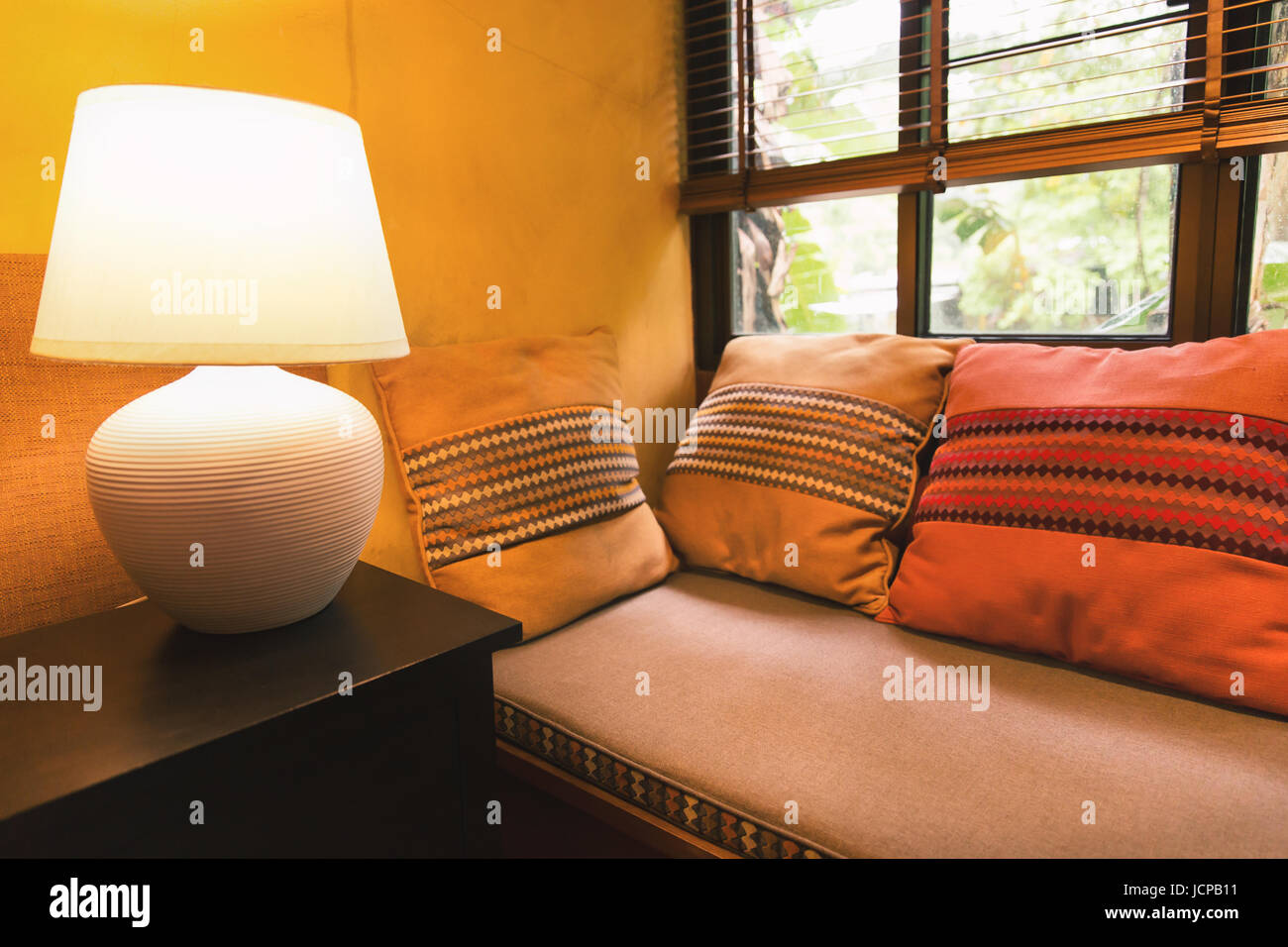 Coin détente de mur jaune chambre avec des coussins sur un canapé-lit et grande table lumineuse lampe sur près de fenêtre claire couverts par rideau. Banque D'Images