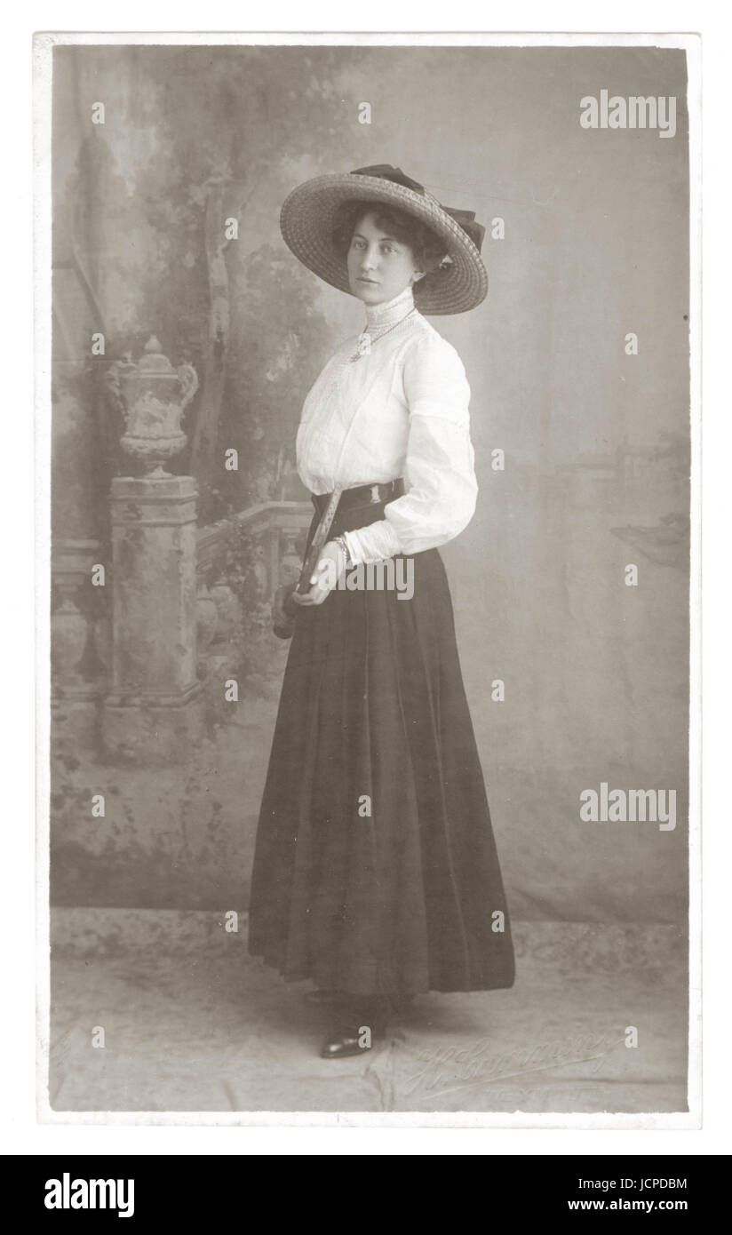 Carte postale, portrait studio de jolie jeune femme édouardienne élégante et glamour portant un grand chapeau à large bord et un chemisier blanc à col haut et une jupe typiques de l'époque, tenant une raquette de tennis, vers 1910, Weymouth, Dorset, Royaume-Uni Banque D'Images