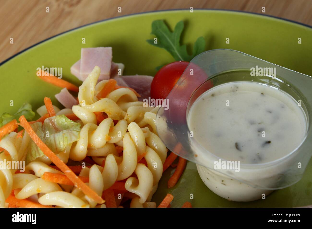 Une salade de pâtes accompagné d'une tomate et un pot de sauce dans une assiette Banque D'Images