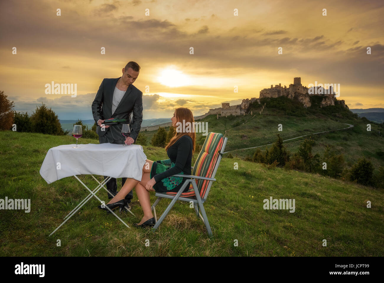 Couple in love boire du vin rouge dans la nature sous les ruines d'un château au coucher du soleil. Banque D'Images