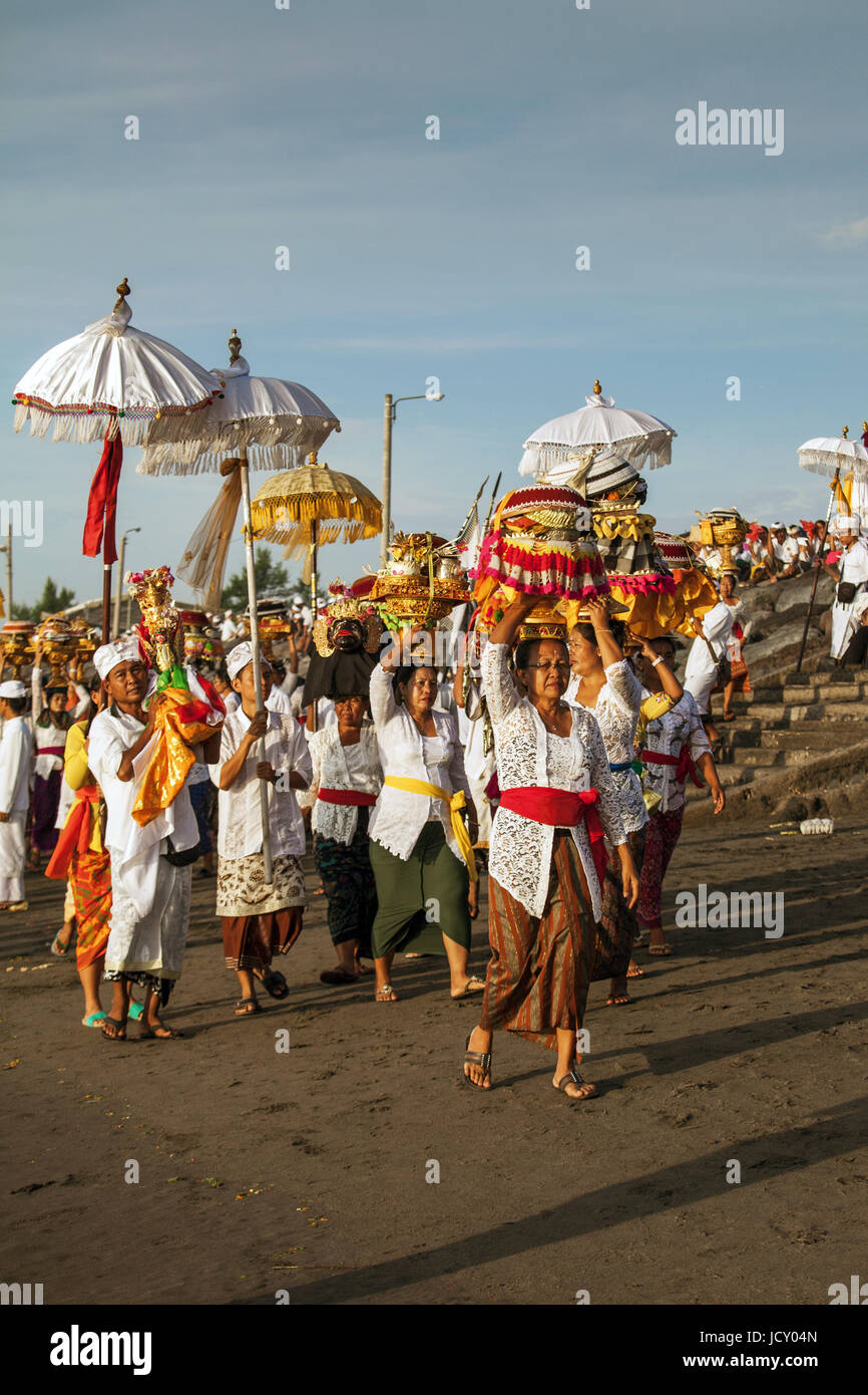 Melasti, rituel balinais annuel cérémonie sur la plage à Bali avec groupe de personnes transportant des parasols colorés et offrandes religieuses sur leurs têtes sur la plage Banque D'Images