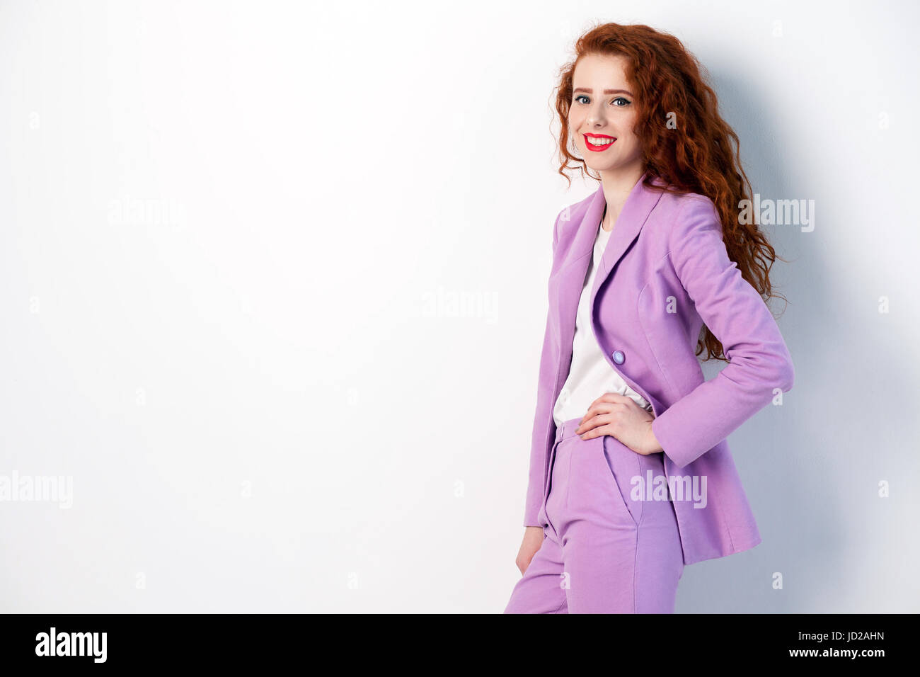 Portrait de femme d'affaires réussie happy - rouge avec les cheveux bruns et un miroir en rose costume. à la caméra avec le sourire à pleines dents, studio shot Banque D'Images