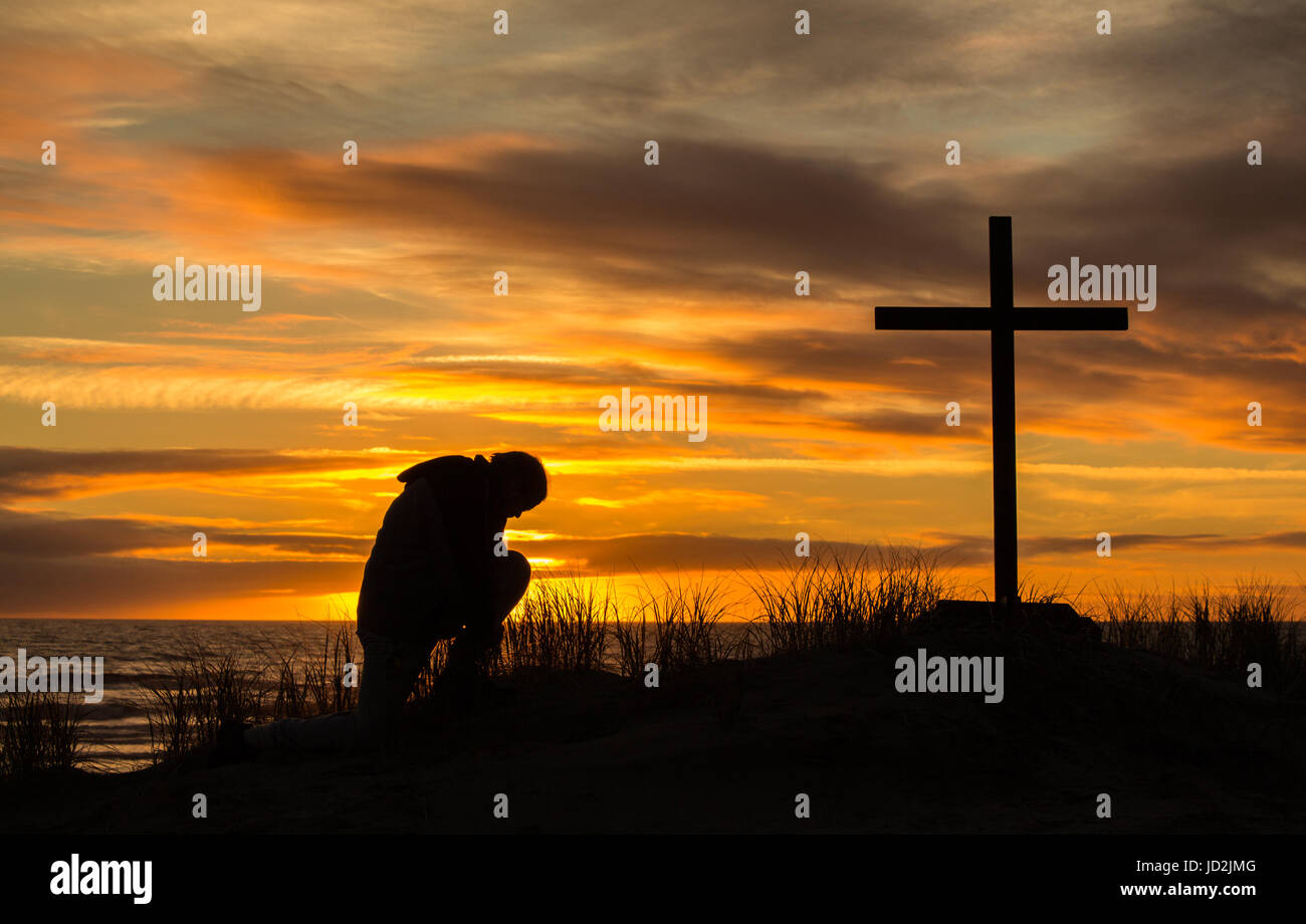 Magnifique coucher de soleil que l'homme s'incline à prier Dieu devant une croix. Banque D'Images