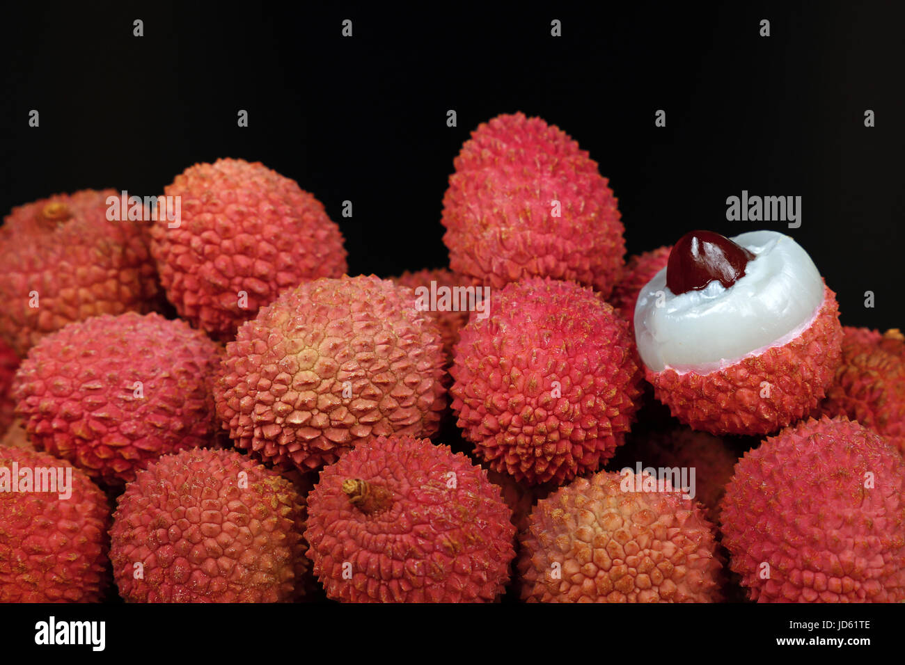 Heap a rouge mûre de litchee (Litchi chinensis) fruits tropicaux avec un litchi ouvrir et pelées, isolé sur fond noir, Close up, bas Banque D'Images