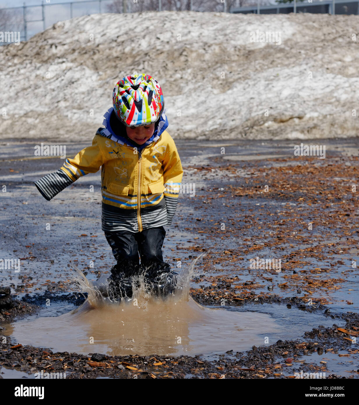 Un jeune garçon (5 ans) sauter dans une flaque boueuse. Banque D'Images