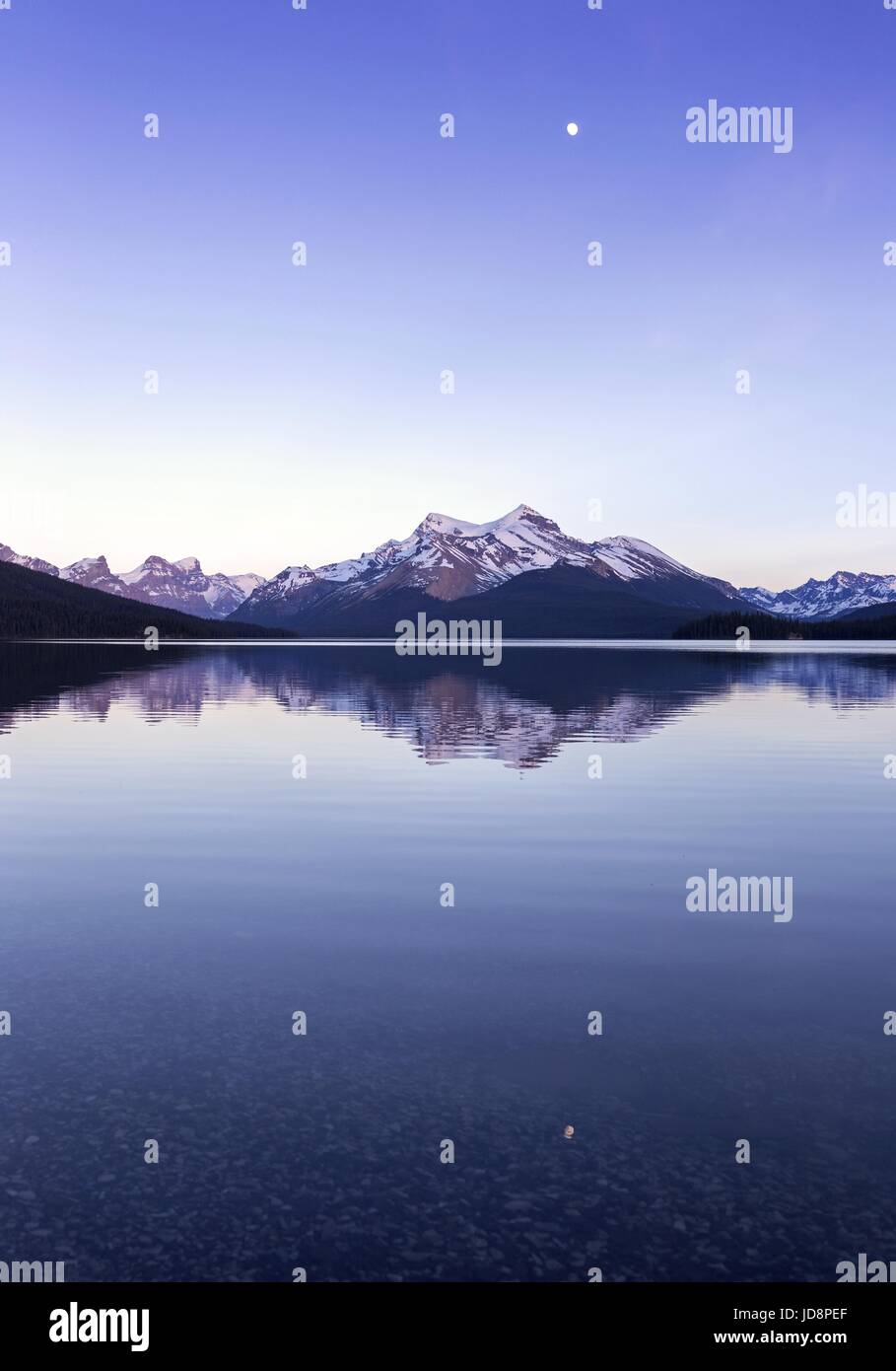 Pleine lune au-dessus de l'eau calme du lac maligne. Ciel nocturne Portrait horizon paysage des montagnes Rocheuses. Parc national Jasper randonnée Rocheuses canadiennes Alberta Banque D'Images