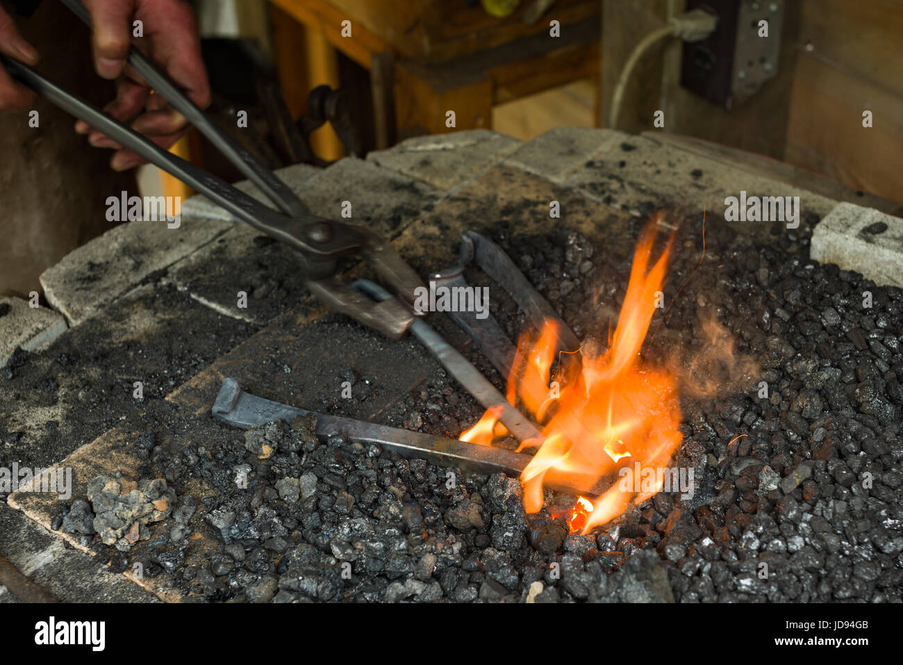 Chauffage forgeron et en tournant avec une pince en acier l'acier dans le charbon de forge en atelier Banque D'Images