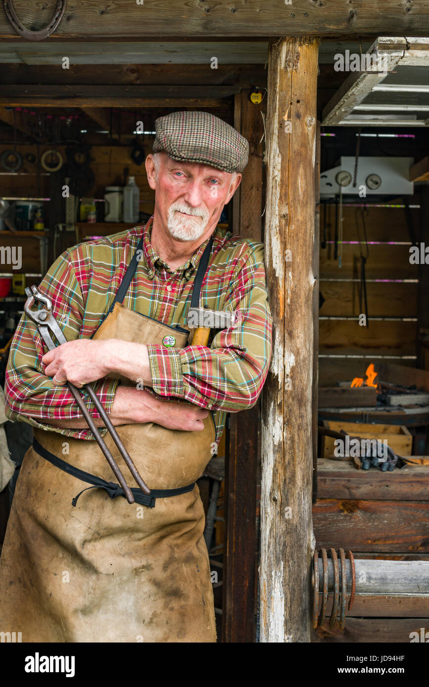 Homme debout à l'extérieur petit forgeron forge et marteau pince tenue de l'atelier Banque D'Images