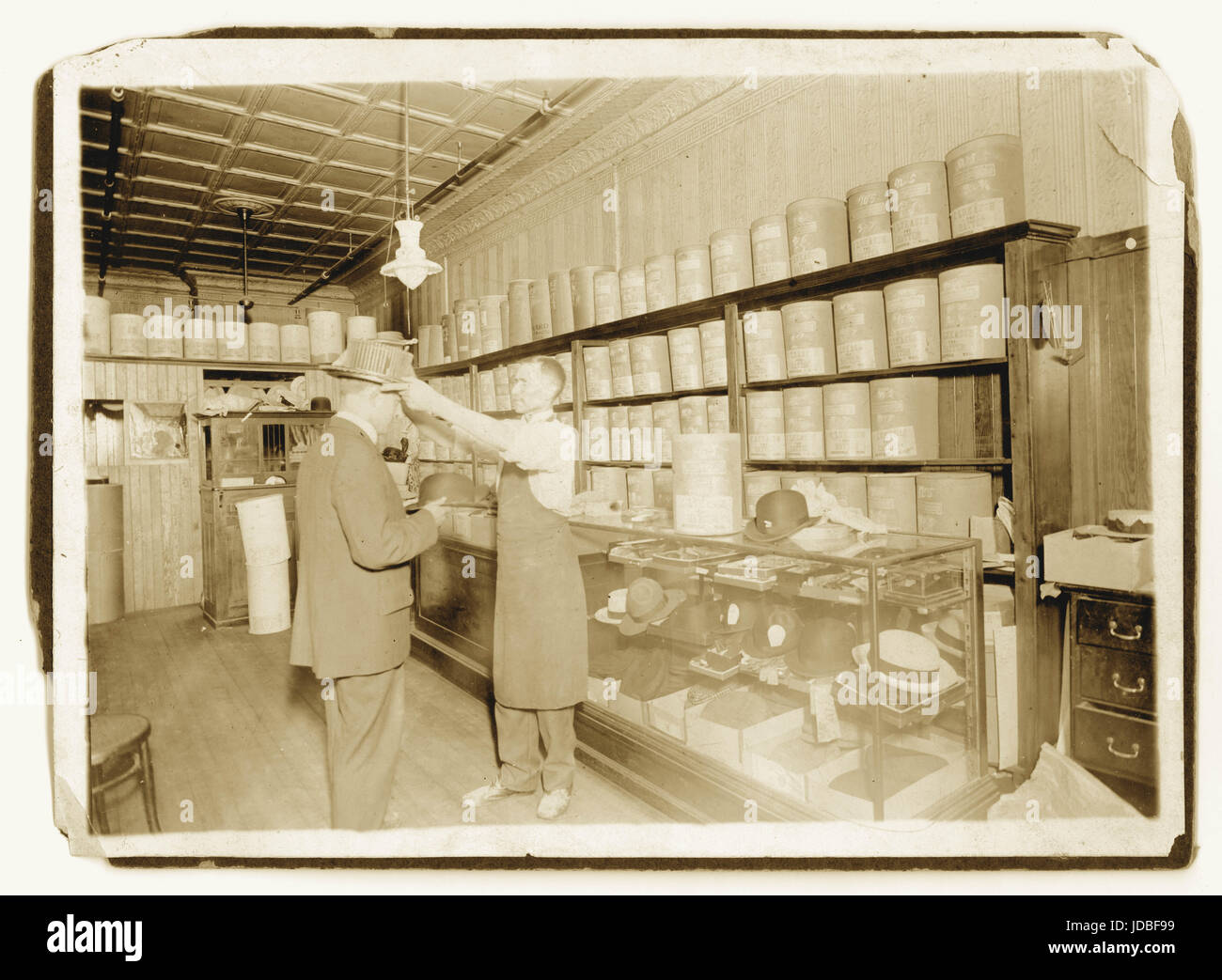 Photo originale du début des années 1900 d'un chapelier / personnel ou assistant, dans l'intérieur d'un magasin victorien, avec un client vendant des chapeaux haut de gamme et des plaisanciers de paille de ses locaux vendant des chapeaux étiquetés dans des boîtes C. Lukasch The Hatter, Royaume-Uni Banque D'Images