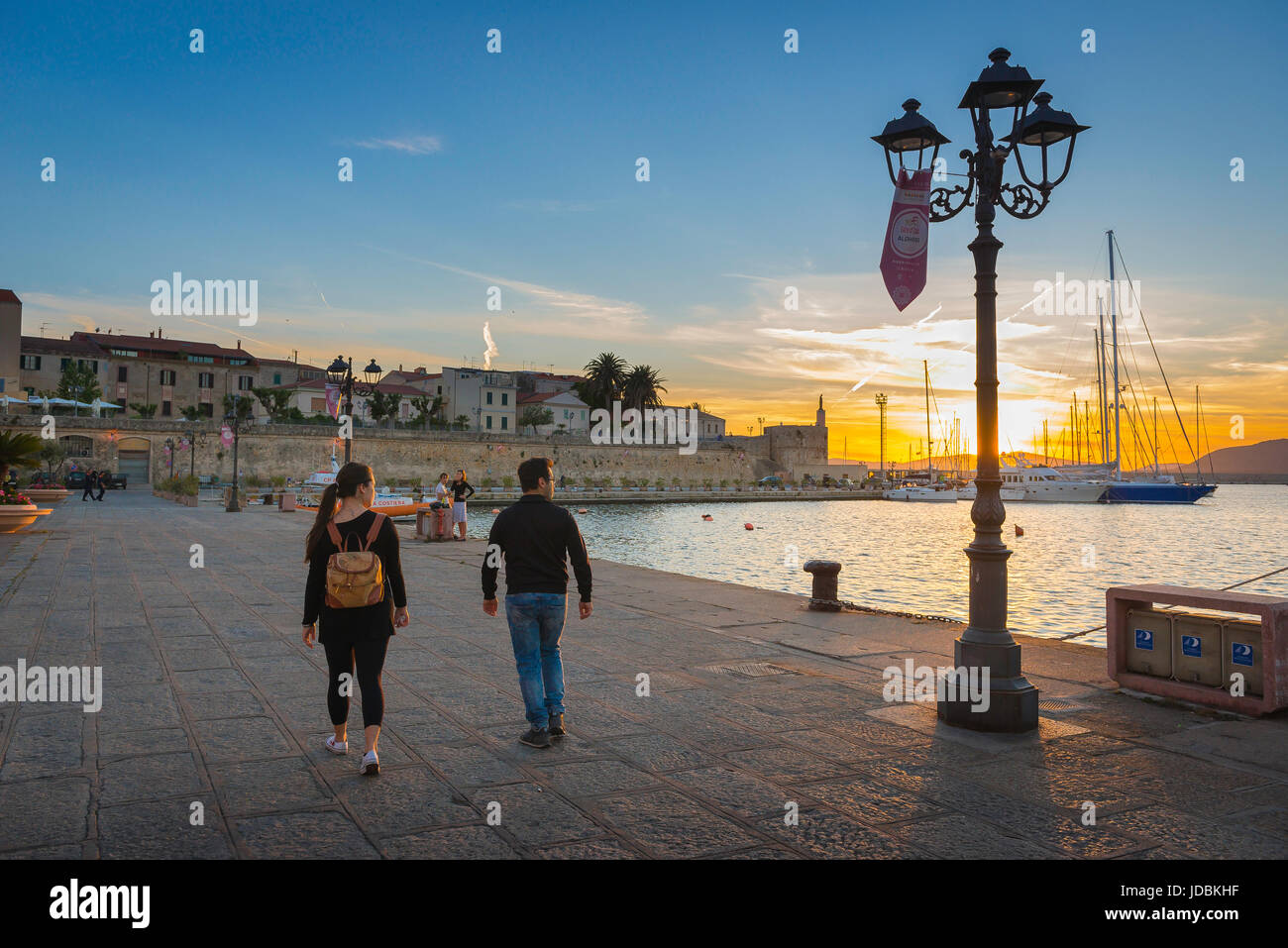 Couple port méditerranéen, un jeune couple regarde un coucher de soleil comme ils marchent le long du front de mer à Alghero, Sardaigne du nord. Banque D'Images