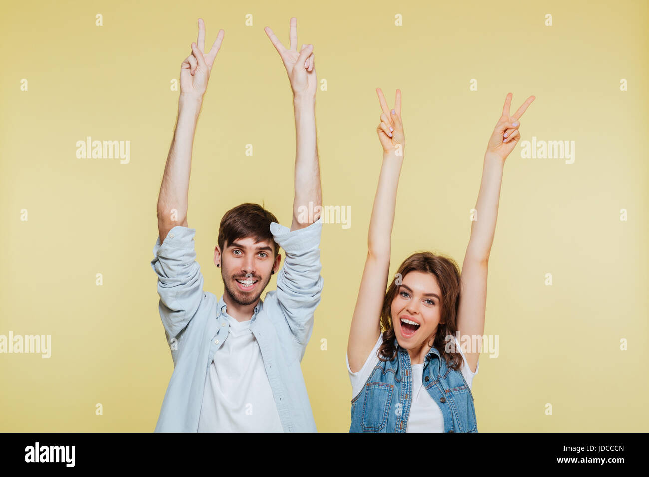 Photo de happy brother and sister montrant la paix sur fond jaune. À la caméra. Banque D'Images