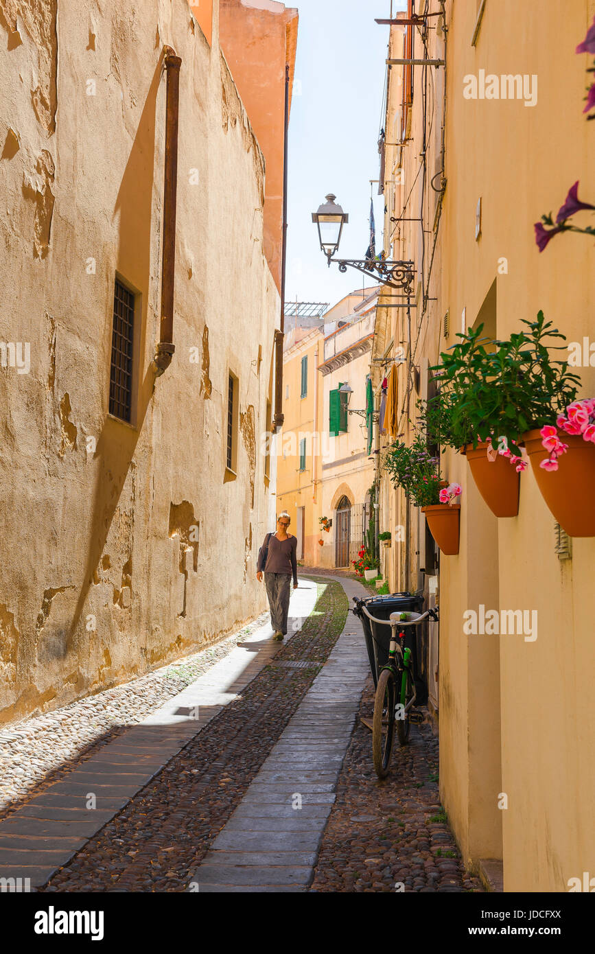 Femme solo Voyage concept, vue d'une femme marchant seule dans une rue étroite dans le quartier de la vieille ville d'Alghero, Sardaigne, Italie. Banque D'Images