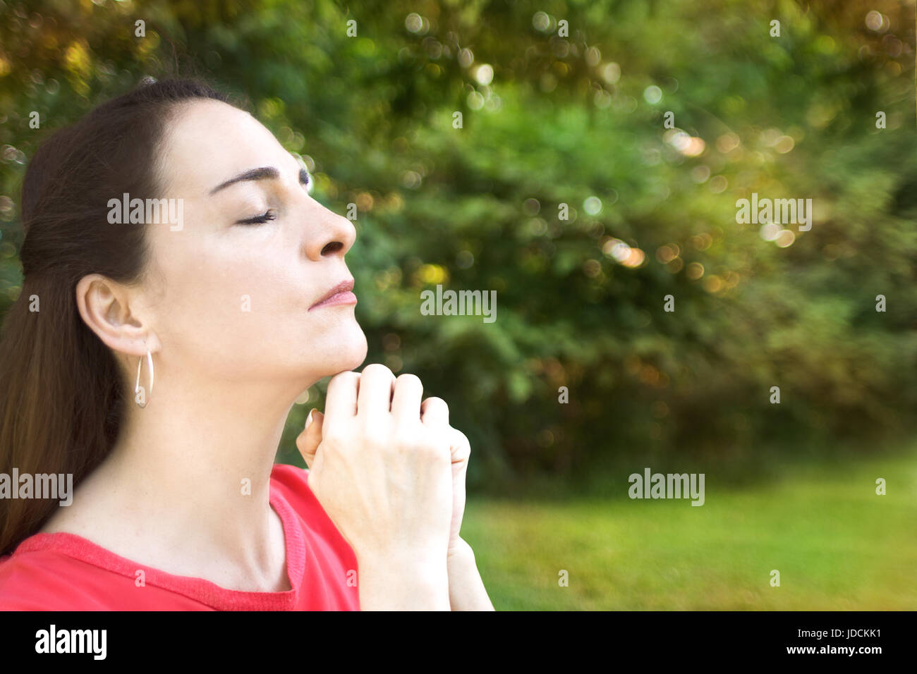 Portrait d'une femme à l'extérieur, fermé les yeux et les mains ensemble, qui souhaitent, en priant. Banque D'Images