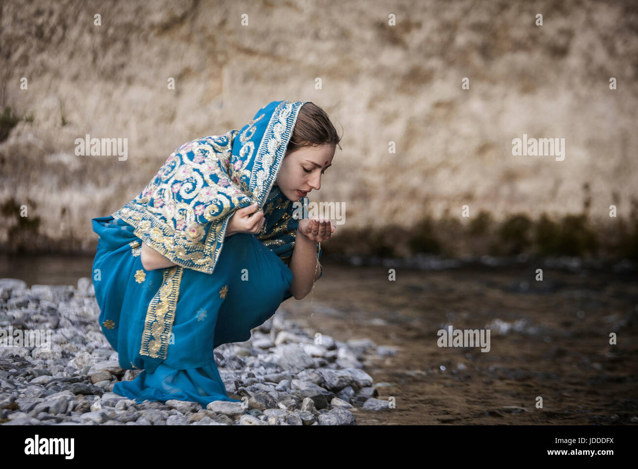 La fille dans le sari indien assis à la petite rivière et des boissons de mains Banque D'Images