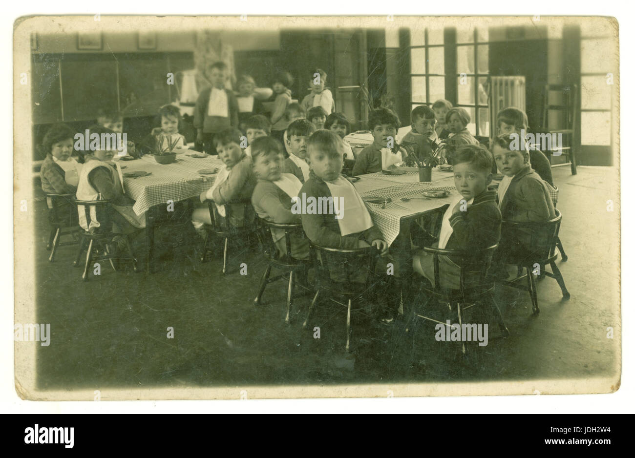 Carte postale du début des années 1900 : des bébés d'âge maternelle ou primaire s'assoyent à des tables pour le petit déjeuner, le dîner ou un en-cas, portant des serviettes, au Royaume-Uni Banque D'Images