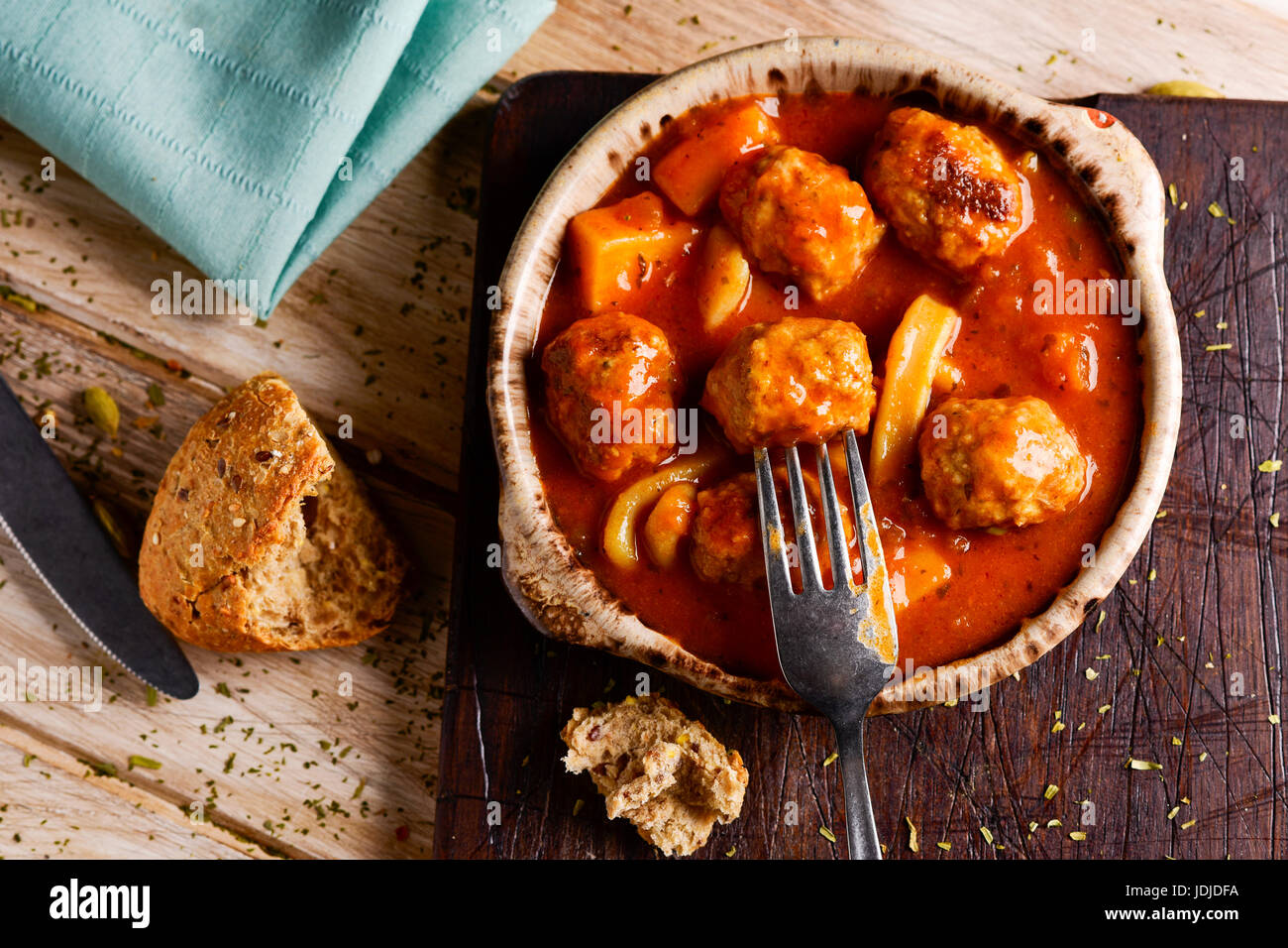 Capture d'un grand angle d'un bol en terre cuite typique espagnole avec albondigas con sepia, boulettes de viande avec de la seiche, un morceau de pain, une fourchette et un couteau sur un Banque D'Images