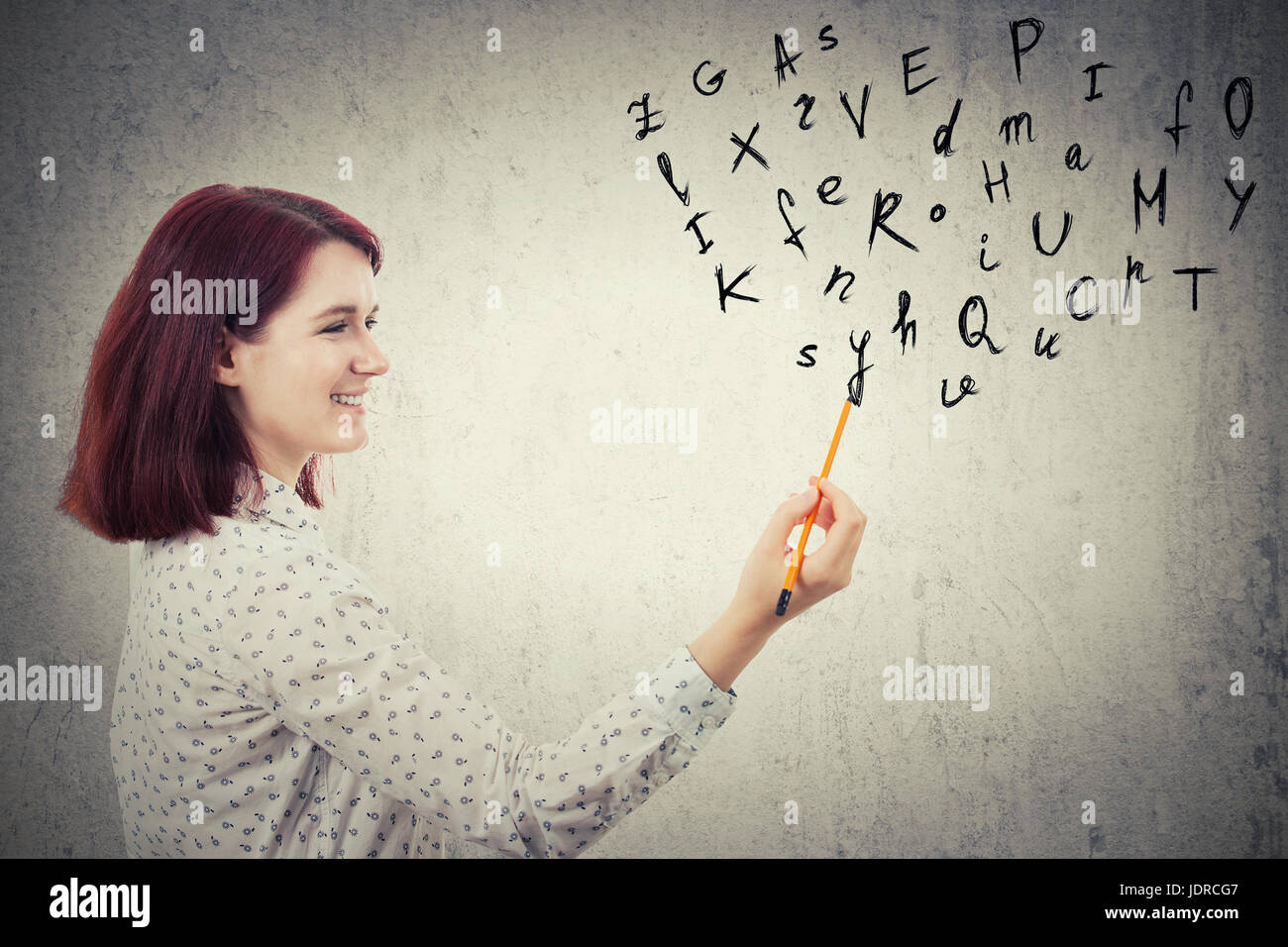 Jeune femme d'affaires, tenant un crayon dans sa main, le dessin des lettres de l'alphabet. L'éducation et communication concept isolé sur fond de mur gris. Banque D'Images