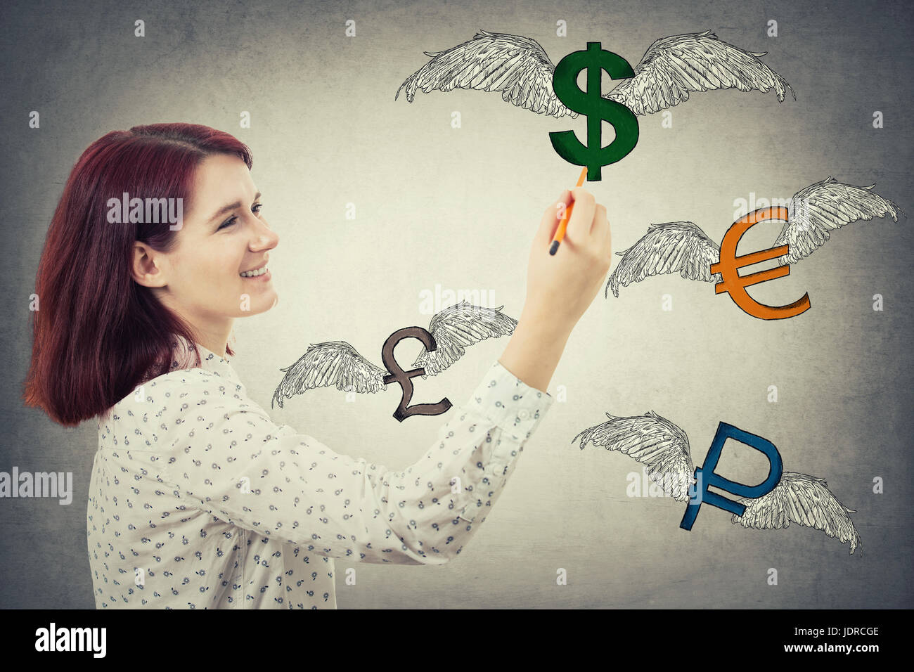 Young businesswoman holding un crayon dans sa main, le dessin des signes d'argent ailé, comme dollar, euro, livre et ruble volent loin isolé sur mur gris b Banque D'Images