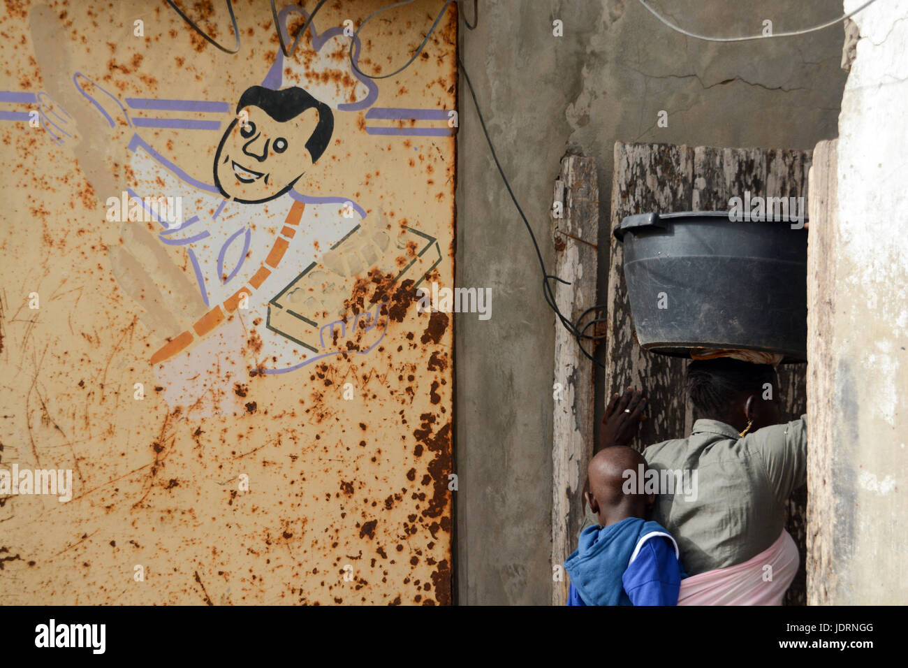 Dessin d'un cuisinier sur le mur rouillé. Femme Sénégalaise est porteur d'un seau en plastique sur la tête et a un enfant fixée à l'arrière. Yoff, Dakar, Sénégal Banque D'Images