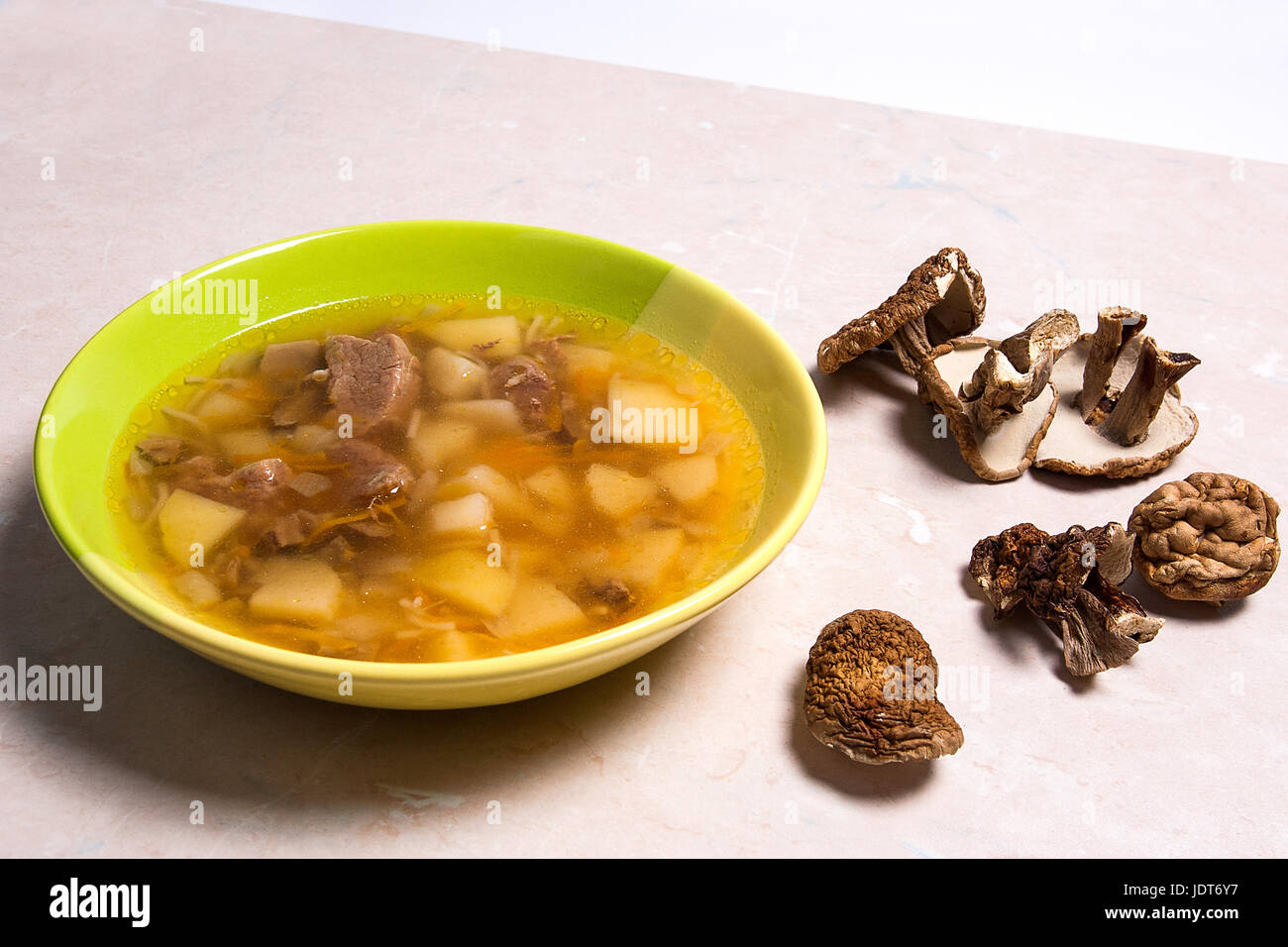 Soupe aux champignons en plaque verte sur un fond noir en lumière. Cèpes séchés plusieurs champignons sauvages ou blanc sur tissu marron. Banque D'Images