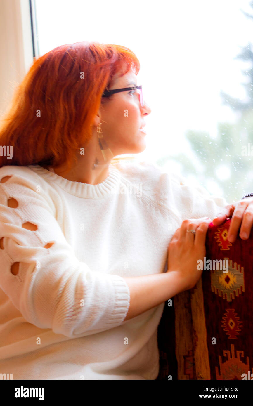 Jolie jeune femme regardant par la fenêtre, dans sa solitude Banque D'Images