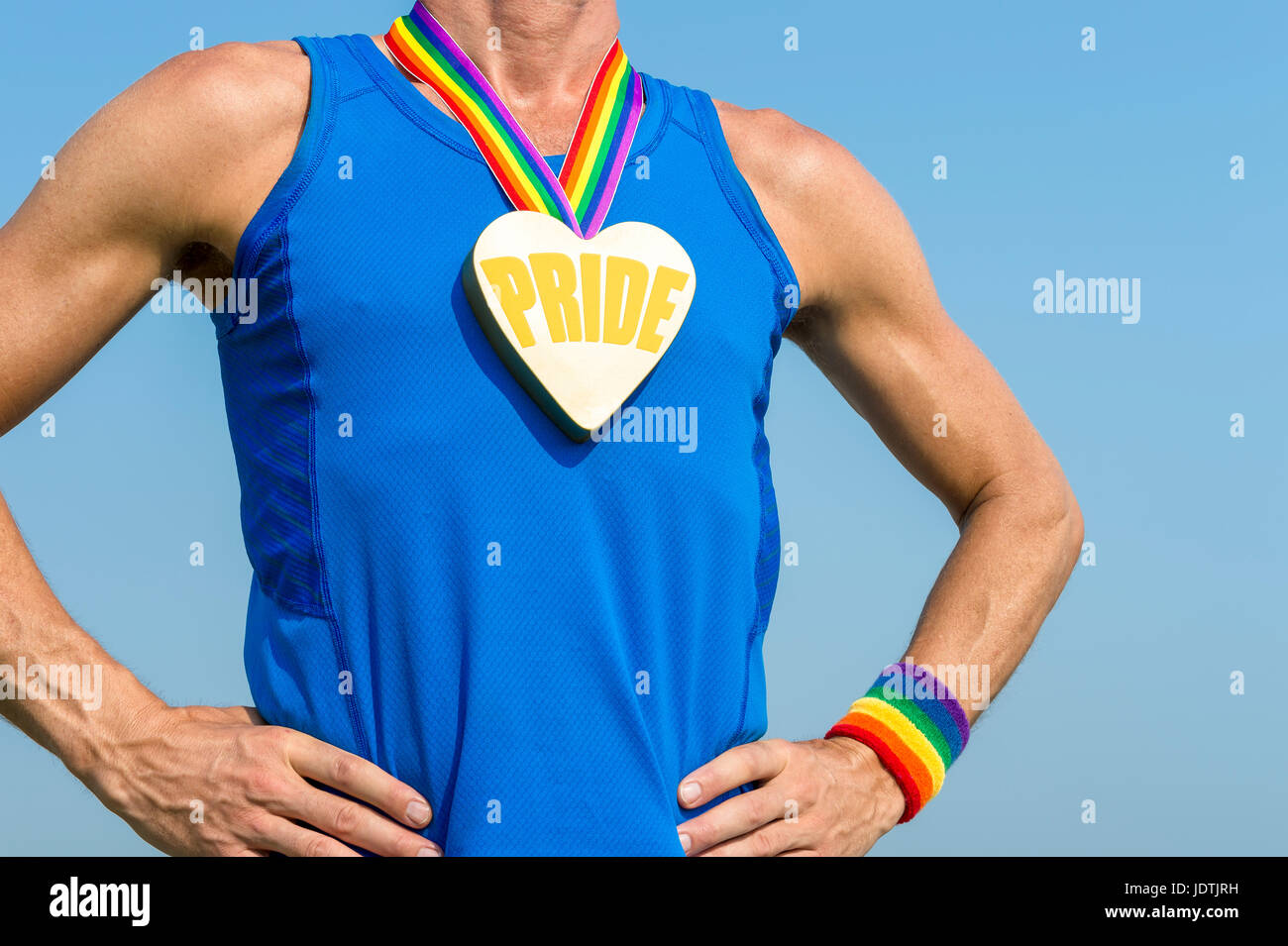 Comité permanent de l'athlète gay pride avec coeur médaille d'or et ruban arc-en-ciel contre ciel bleu Banque D'Images