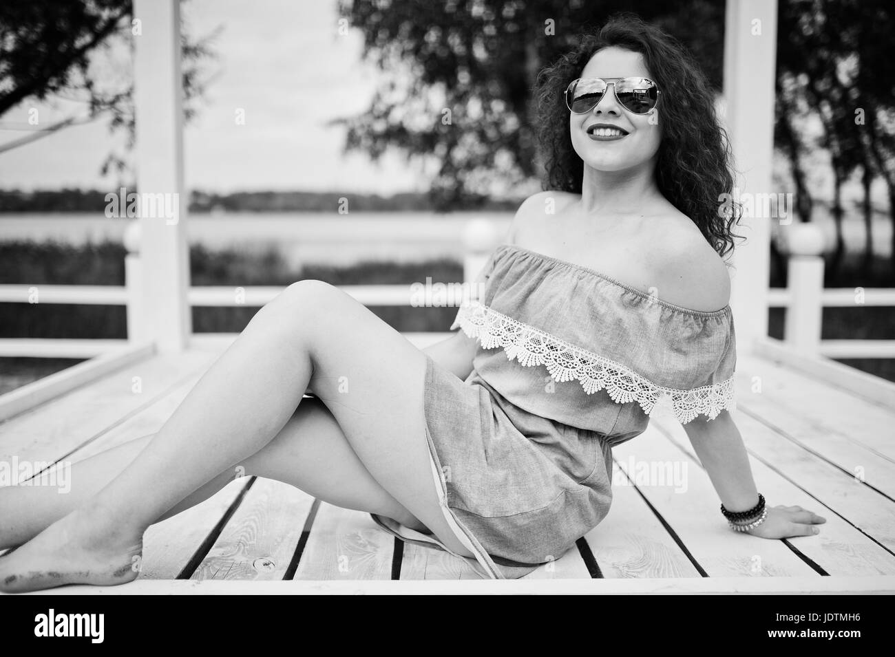 Portrait d'une jeune fille portant des vêtements chic posant sur une terrasse en bois blanc. Photo en noir et blanc. Banque D'Images