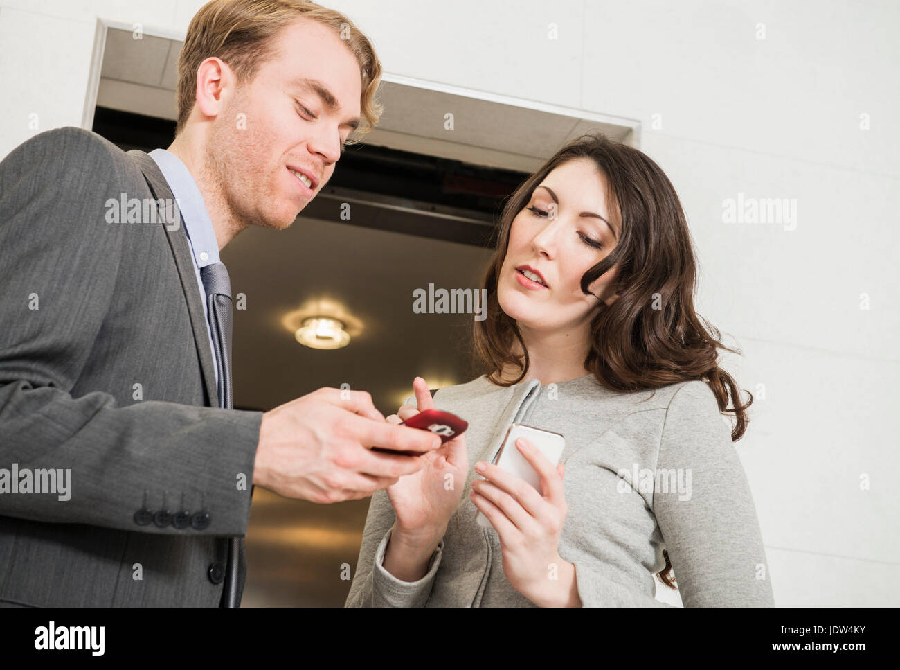 Office colleagues using cell phone par ascenseur Banque D'Images