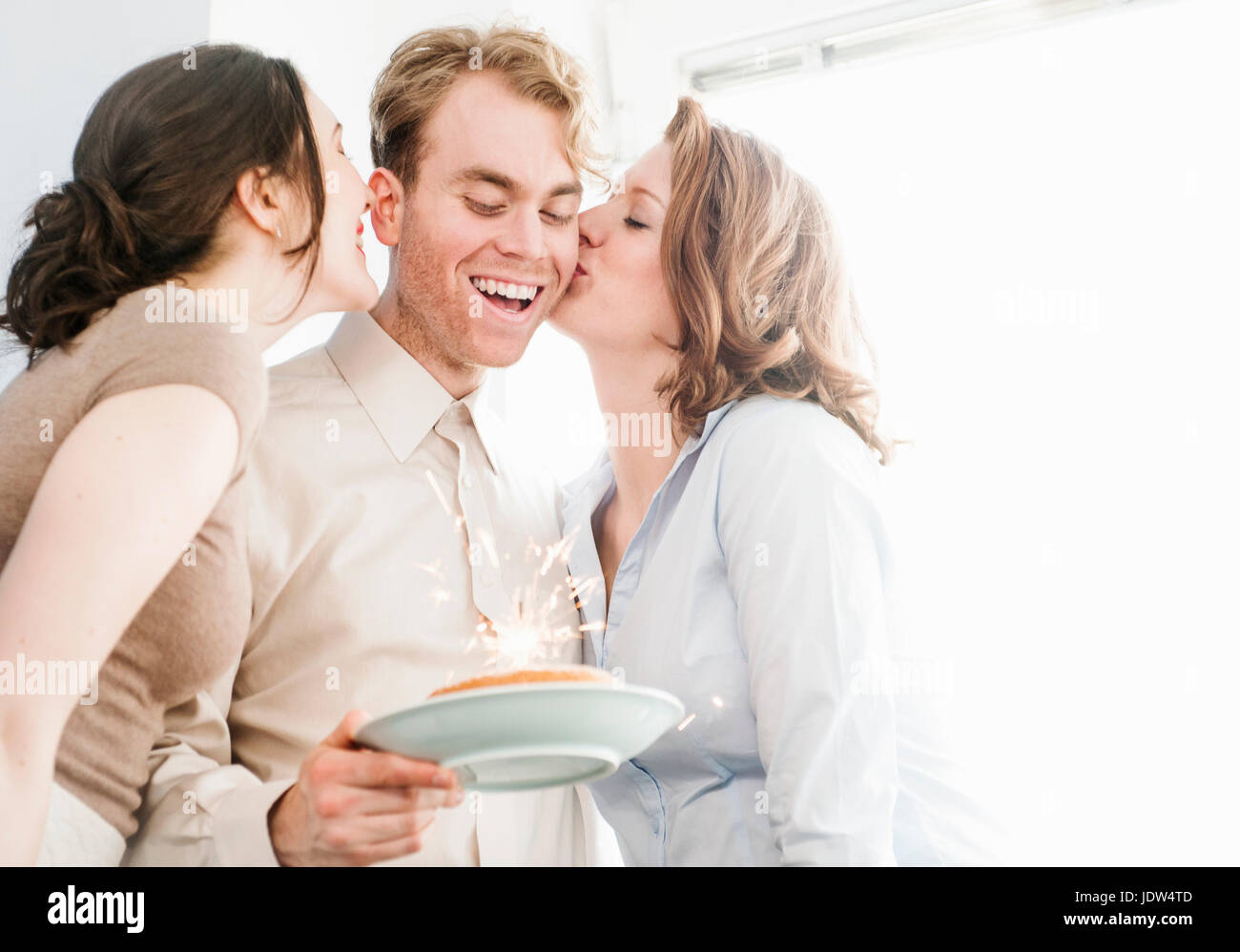 Collègues femmes kissing man on cheek with birthday cake Banque D'Images