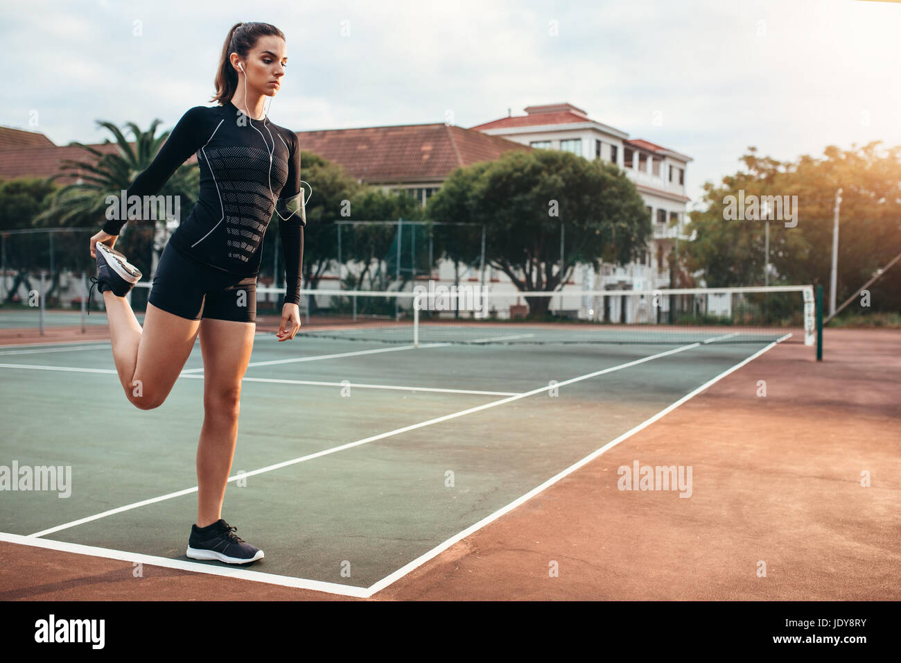 Portrait d'une athlète qui s'étend à l'extérieur de la jambe. Belle femme exerçant sur un court de tennis. Banque D'Images