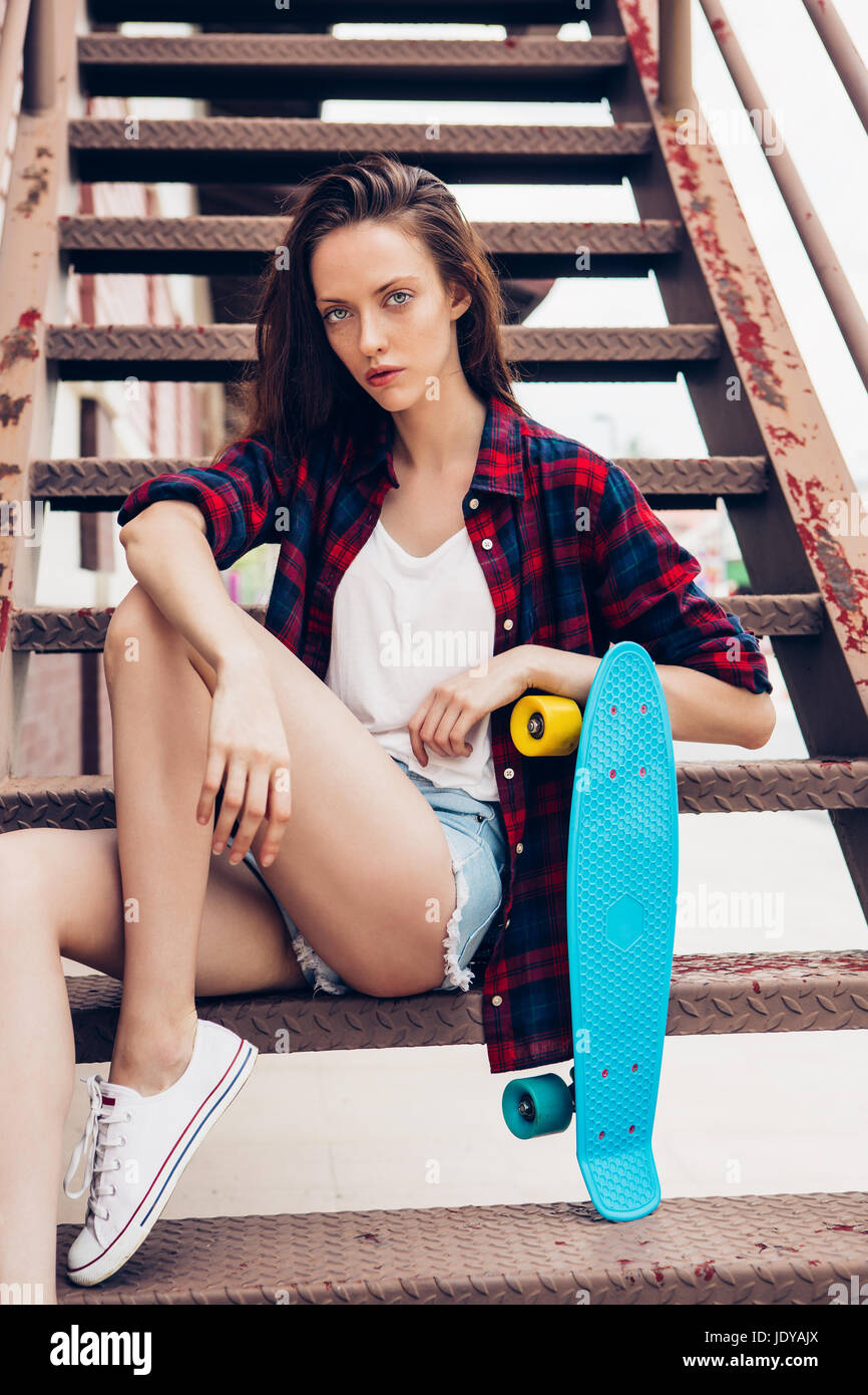 Belle jeune fille en chemise à carreaux, jeans taille basse short shorts et baskets  blanches s'asseoir sur l'escalier avec mini bleu Longboard skate board. S  urbaines Photo Stock - Alamy