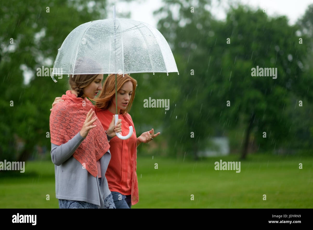 Deux femmes marchant park dans la pluie et de parler. L'amitié et les gens de la communication. Banque D'Images